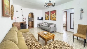 A living room with a sofa, a coffee table, and a chair. There is a TV on the wall and a fireplace.