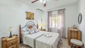 A bedroom with a bed, bedside tables, a lamp, a window with curtains, and a wall-mounted air conditioner.