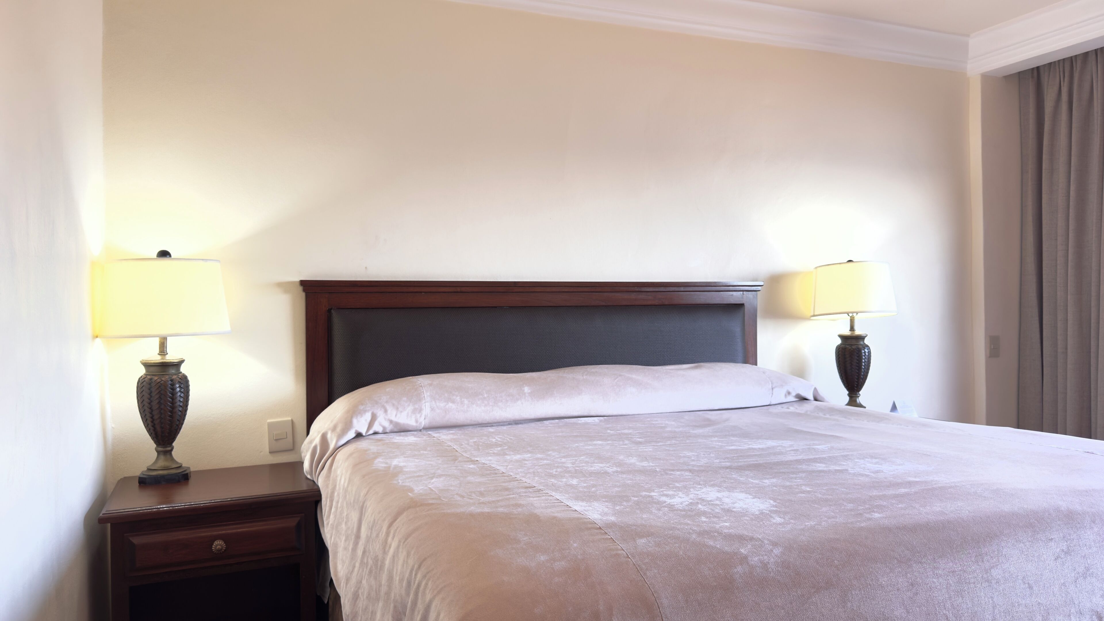 Habitación de hotel con una cama grande, dos lámparas de noche, un cabecero de madera y una mesita de noche.