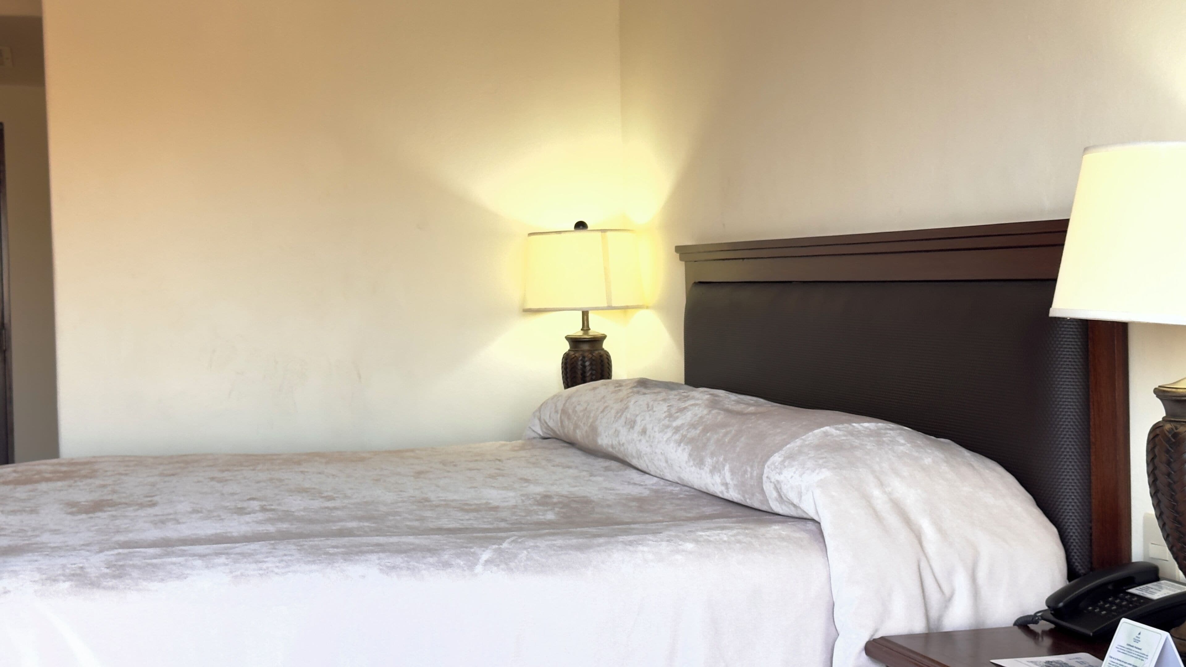A hotel room with a bed, a nightstand with a lamp, and a telephone.