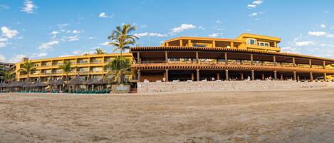 A beachfront hotel with multiple balconies, a covered outdoor area, and a sandy beach.