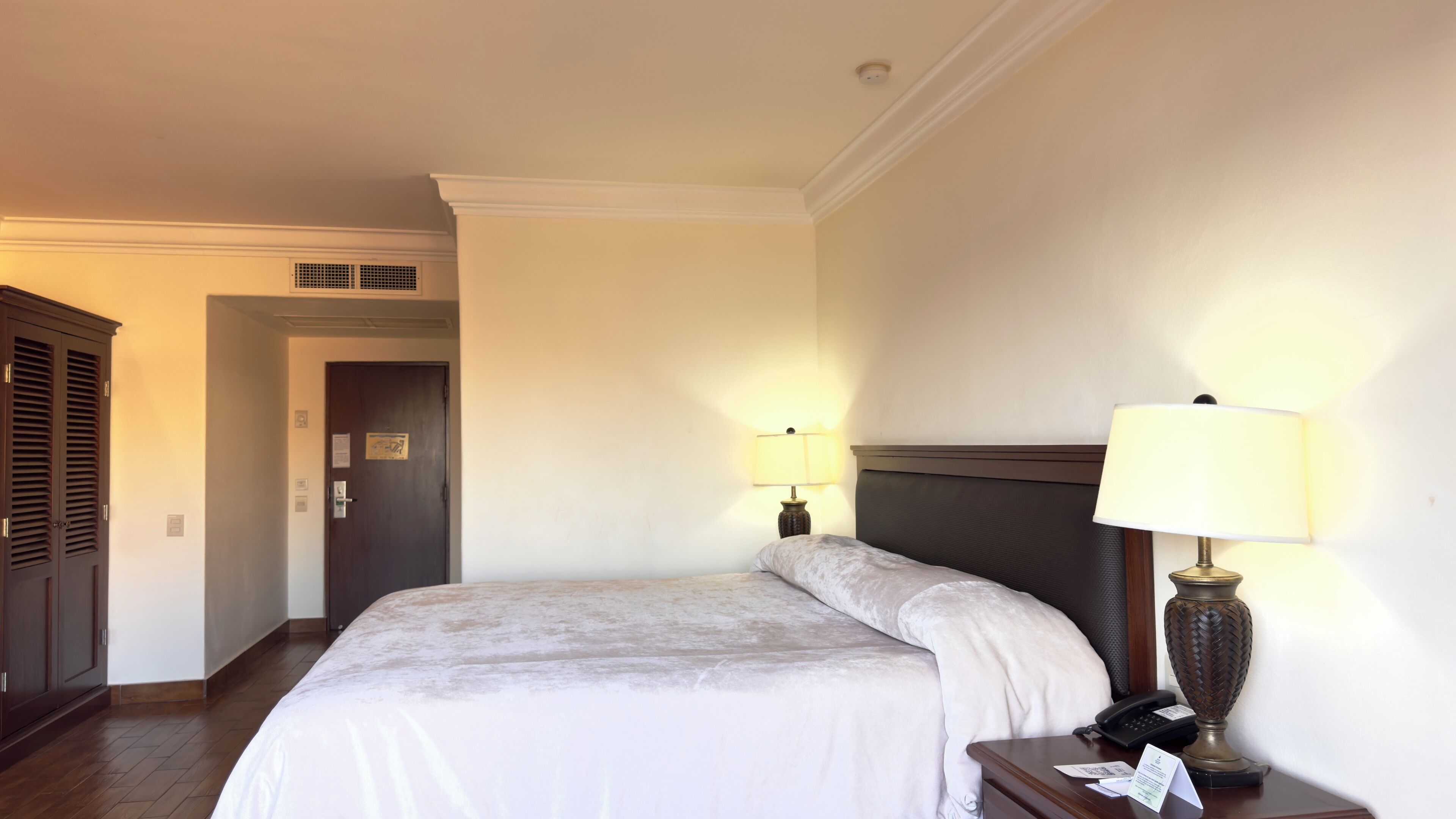 A hotel room with a bed, bedside lamps, a nightstand, a telephone, and a door to the hallway.