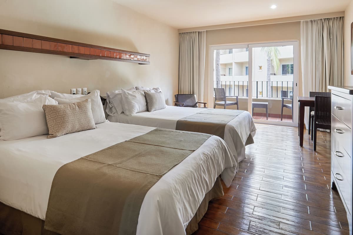 A hotel room with two beds, a balcony with a view, a desk, and a chair.
