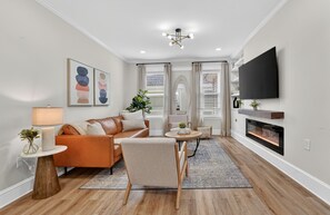Una sala de estar con sofá, sillón, mesa de centro, televisión, chimenea y obras de arte.