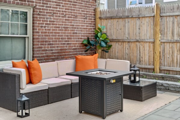 A patio with a sofa, cushions, a table, and a lantern.