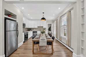 A modern kitchen with white cabinets, a stainless steel refrigerator, and a dining area with a wooden table and chairs.