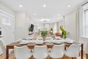 A dining area with a wooden table set for six, white chairs, and a potted plant.