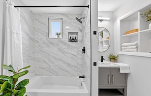 A modern bathroom with a bathtub, a shower, a sink, and a mirror.