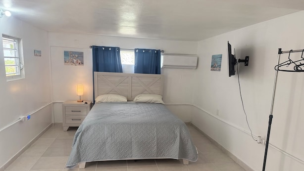 A bedroom with a bed, a nightstand, a lamp, a wall-mounted air conditioner, and a clothes drying rack. - The residence 2 (Cabo Rojo)