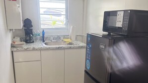 A compact kitchen with a refrigerator, microwave, coffee maker, and a window with blinds. - The residence 2 (Cabo Rojo)