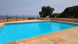 Ein rechteckiger Pool mit Fliesen umgeben, mit einer Umzäunung und Bäumen im Hintergrund.