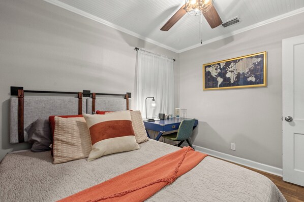 A bedroom with a bed, a desk, a chair, a world map on the wall, and a ceiling fan.