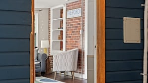 Una habitación acogedora con pared de ladrillo, una silla blanca, una mesita pequeña y un letrero que dice "The Porch".