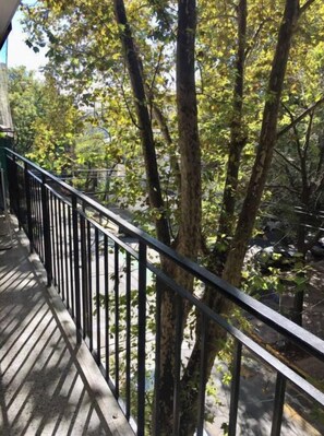 A wooden deck with a metal railing overlooking a forested area.