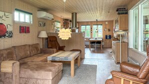 A cozy living room with a brown leather sofa, a wooden coffee table, and a dining area with a wooden table and chairs.