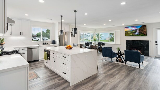 A modern kitchen with white cabinetry, a central island, and a dining area with a fireplace. - Newly Renovated! OC Retreat Near Disney & Beaches (Fountain Valley)