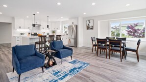 A modern kitchen with white cabinets, stainless steel appliances, and a dining area with blue chairs and a table. - Newly Renovated! OC Retreat Near Disney & Beaches (Fountain Valley)