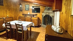 A wooden interior with a dining table, chairs, a television, and a fireplace.