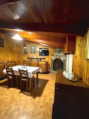 Interior em madeira com mesa de jantar, cadeiras, televisão e lareira.