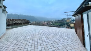 A rooftop terrace with a tiled floor and a view of a cityscape and hills in the distance.