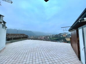 Terraço no telhado com piso de azulejos e vista para a paisagem urbana e colinas ao longe.