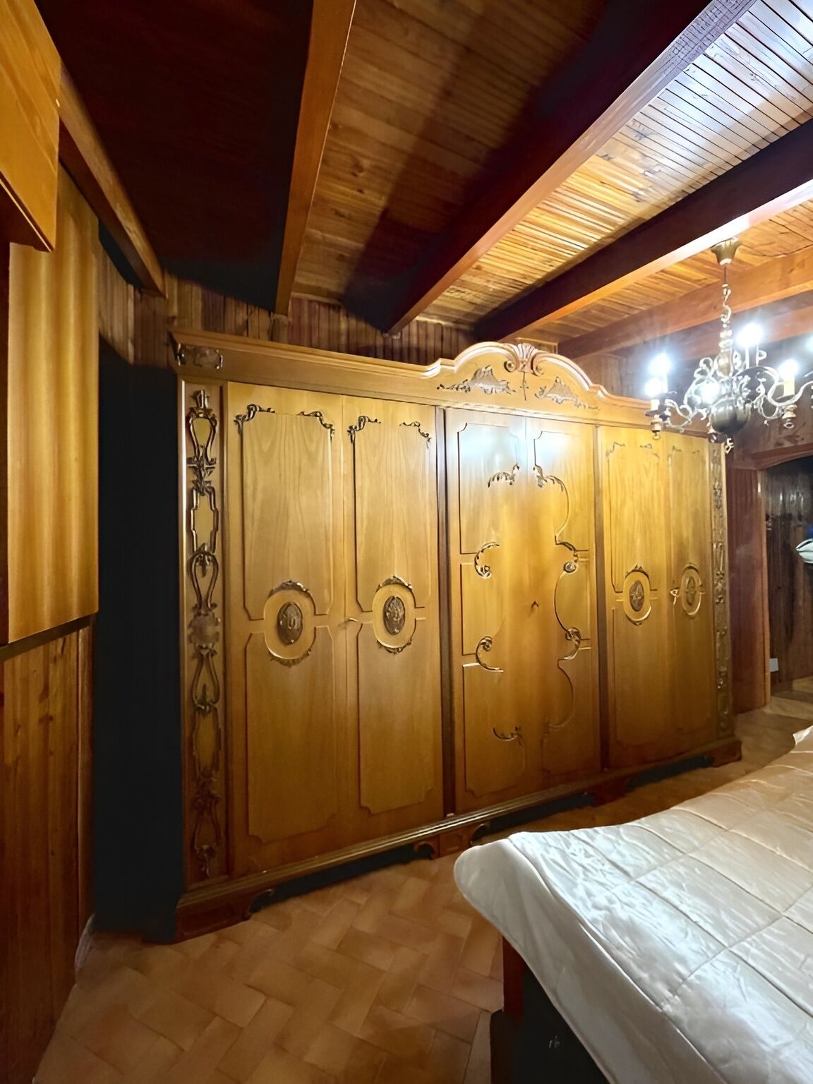 A room with a wooden wardrobe, a bed, and a chandelier.