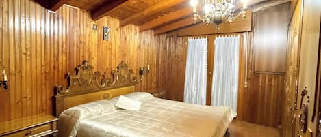 A spacious bedroom with a large bed, wooden walls, and a chandelier.