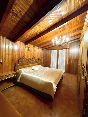Quarto espaçoso com uma cama grande, paredes de madeira e um candelabro.