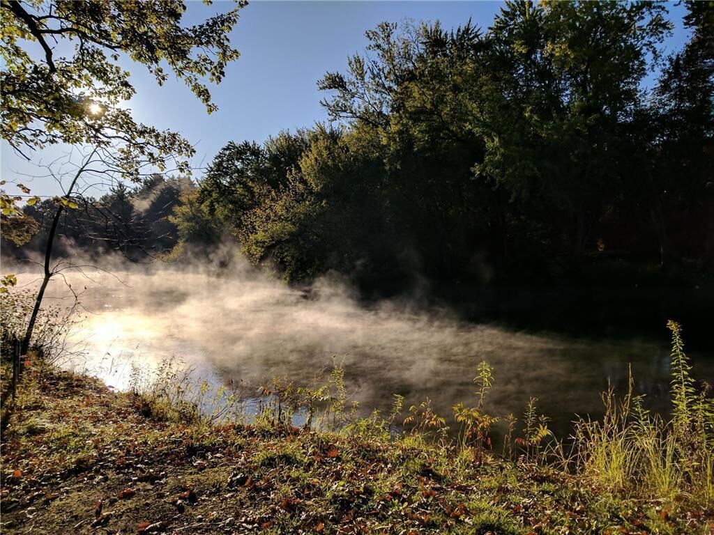 Um lago enevoado rodeado por árvores densas e um céu claro.