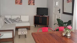 Una sala de estar con un sofá, un televisor, un mueble y una mesa de comedor con sillas.