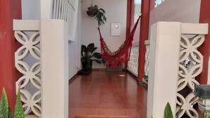 Un pasillo con suelo de baldosas rojas, pilares decorativos blancos y plantas en macetas.