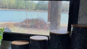 Una habitación con un amplio ventanal que da a una piscina, tres taburetes de diseño elaborado y una planta en maceta.