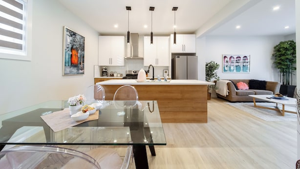 A modern kitchen with a central island, pendant lighting, and a dining area with a glass table.