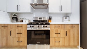 A modern kitchen with white cabinets, a stainless steel stove, and wooden drawers.