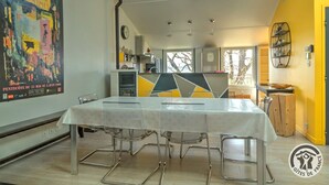 Un comedor con una mesa larga y sillas, una cocina al fondo y un cartel grande en la pared.