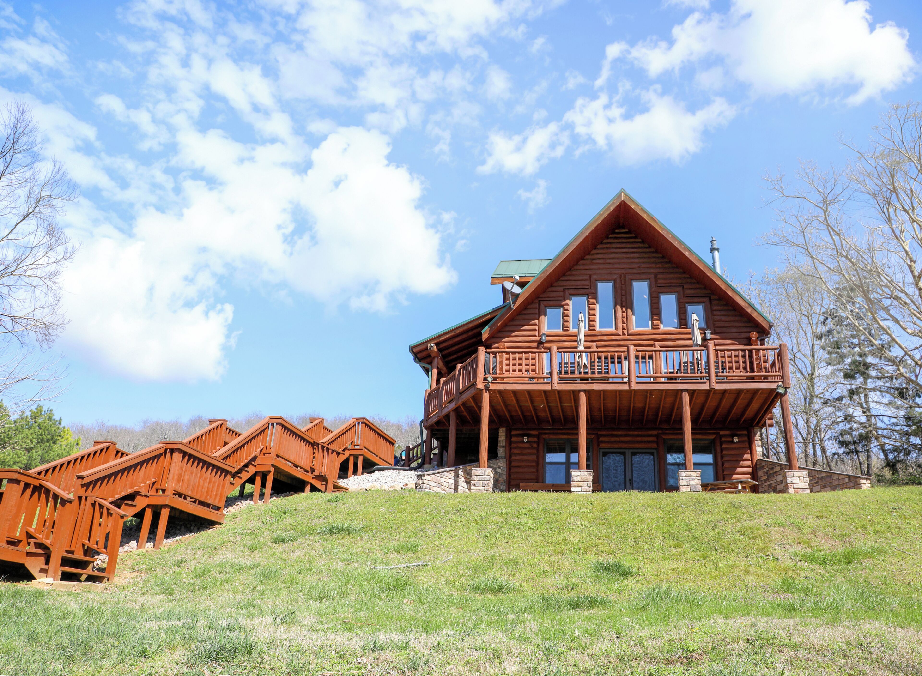 Une grande cabane en rondins dotée d’un balcon, de nombreuses fenêtres et de fondations en pierre.