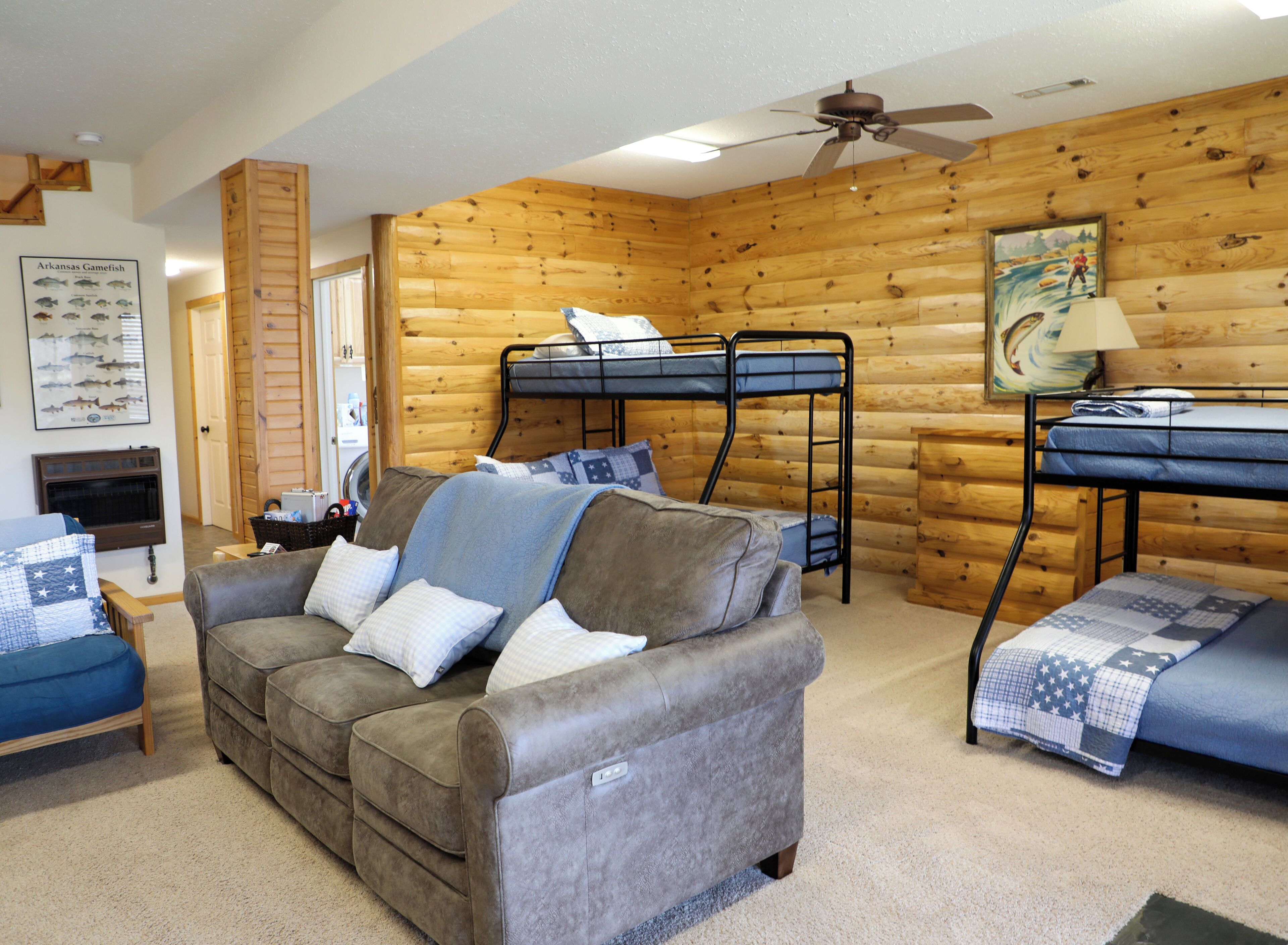 A cozy cabin-style room with a sofa, bunk beds, a desk, and a ceiling fan.