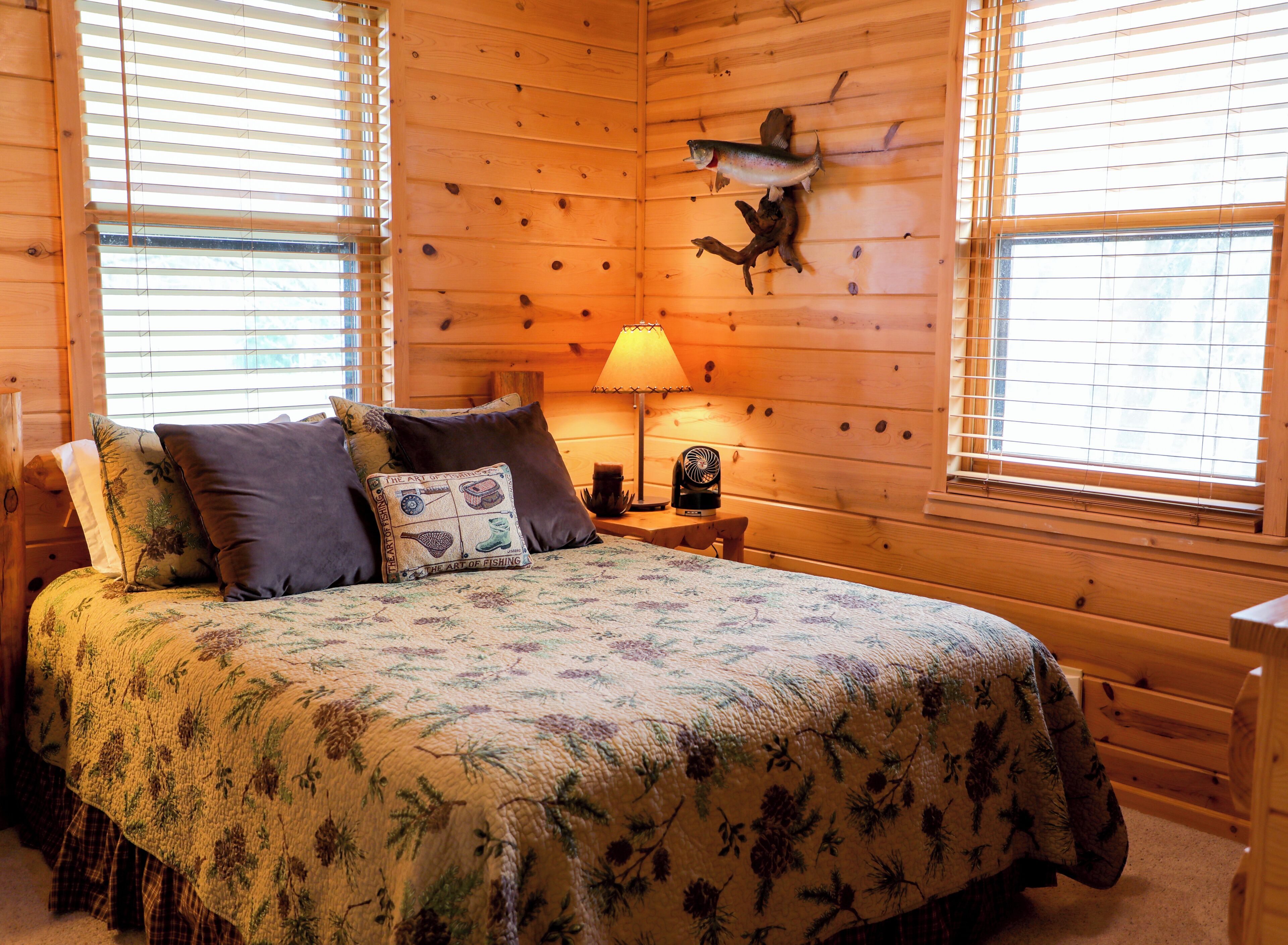 A wooden cabin room with a bed, a lamp, and a fish mounted on the wall.