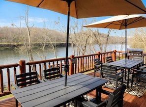 Une terrasse dotée de tables et de chaises, offrant une vue sur un plan d’eau et des arbres.