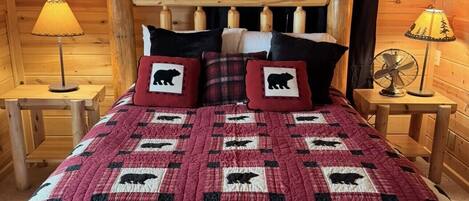 Ein Schlafzimmer einer Holzhütte mit einem Bett, zwei Nachttischen, einer Fischdekoration und einer Decke mit Tiermotiven.