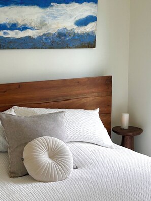 A bed with a wooden headboard, white bedding, and a painting of a blue sky and clouds above.