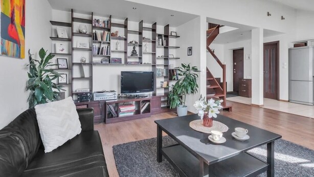Un salon moderne avec un canapé en cuir noir, une table basse et une bibliothèque remplie de livres et d’objets décoratifs.