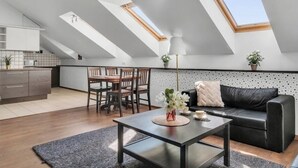 Un appartement moderne de style « loft », doté de fenêtres de toit, d’un coin repas, d’un salon avec un canapé en cuir noir et d’une cuisine aux meubles blancs.
