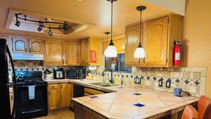 A kitchen with wooden cabinets, a black refrigerator, a microwave, a stove, and pendant lights. - Charming 3-bedroom house with WiFi, fitness/gameroom in Sedona! Serene Backyard! (Sedona)