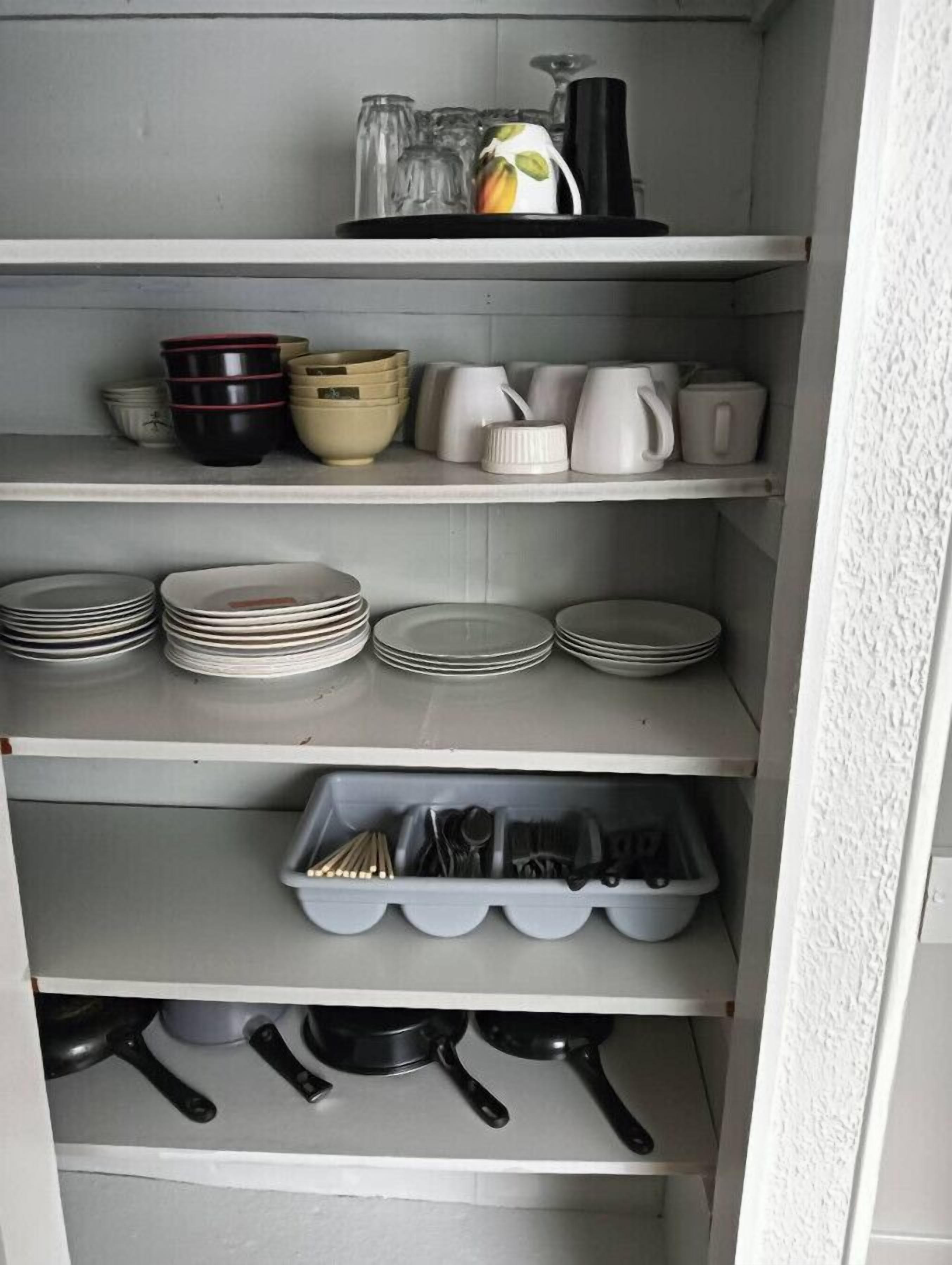 A kitchen with shelves holding plates, bowls, cups, and utensils.