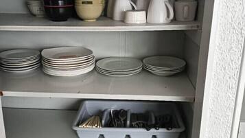 A kitchen with shelves holding plates, bowls, cups, and utensils.