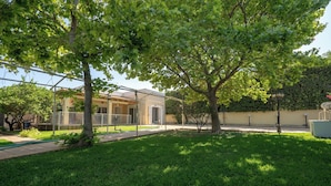 A well-maintained grassy yard with trees and a building in the background. - G&A Family Home near the Beach by MΡS (Nea Makri)