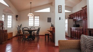 A spacious kitchen with wooden cabinets, a dining area with chairs, a hanging light fixture, and a large window providing natural light. - Rustic Casona w. Seaview, Fire Pit & AC between Cabo Rojo & Lajas (Cabo Rojo)