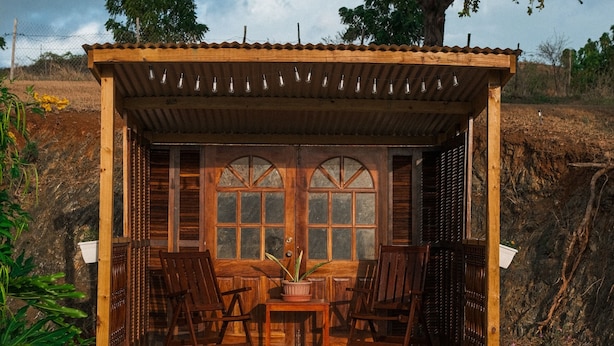 A wooden structure with a covered patio, wooden chairs, a table, and a large window. - Rustic Casona w. Seaview, Fire Pit & AC between Cabo Rojo & Lajas (Cabo Rojo)