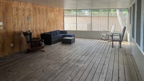 Une terrasse couverte avec un plancher en bois, un canapé de couleur foncée, une petite table et une chaise.